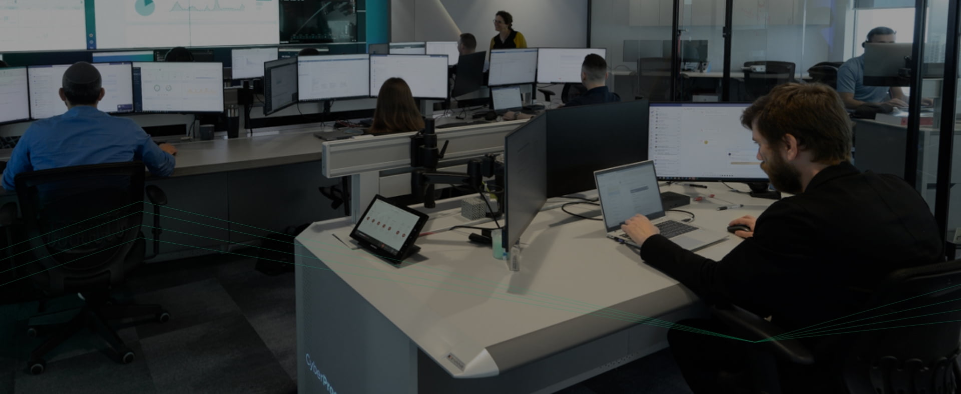 In einer modernen Büroumgebung sind die Mitarbeiter an ihren Schreibtischen mit mehreren Monitoren beschäftigt und verwalten SOC-Aufgaben effizient, um die Sicherheitsabläufe zu verbessern.