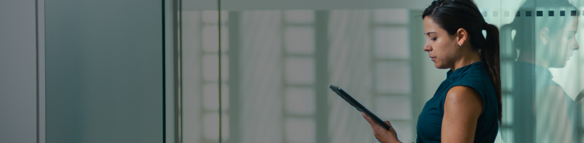 A woman stands next to a glass wall, looking down at a tablet she is holding, checking the latest SIEM updates.