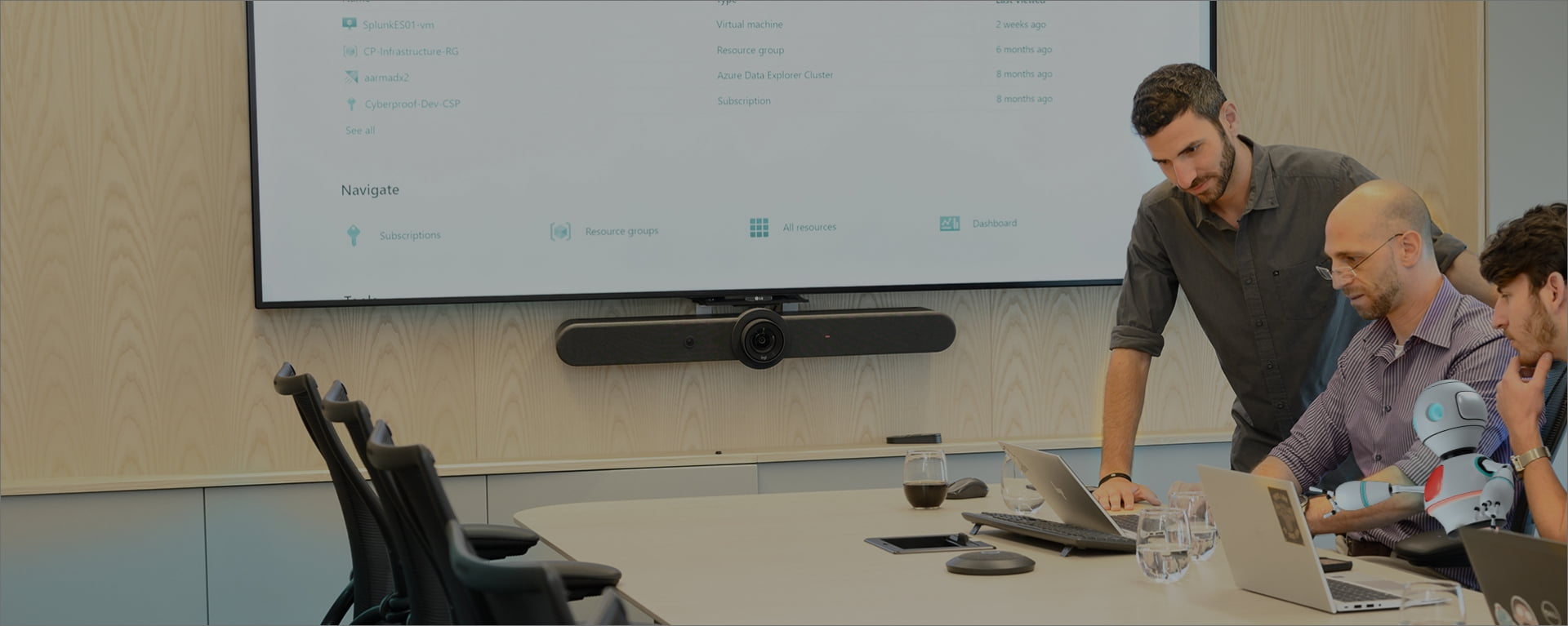 Drei Männer arbeiten zusammen an einem Konferenztisch und überprüfen in einer modernen Büroumgebung Informationen auf einem großen Bildschirm. Dabei nutzen sie verwaltete Erkennungs- und Reaktionstools.