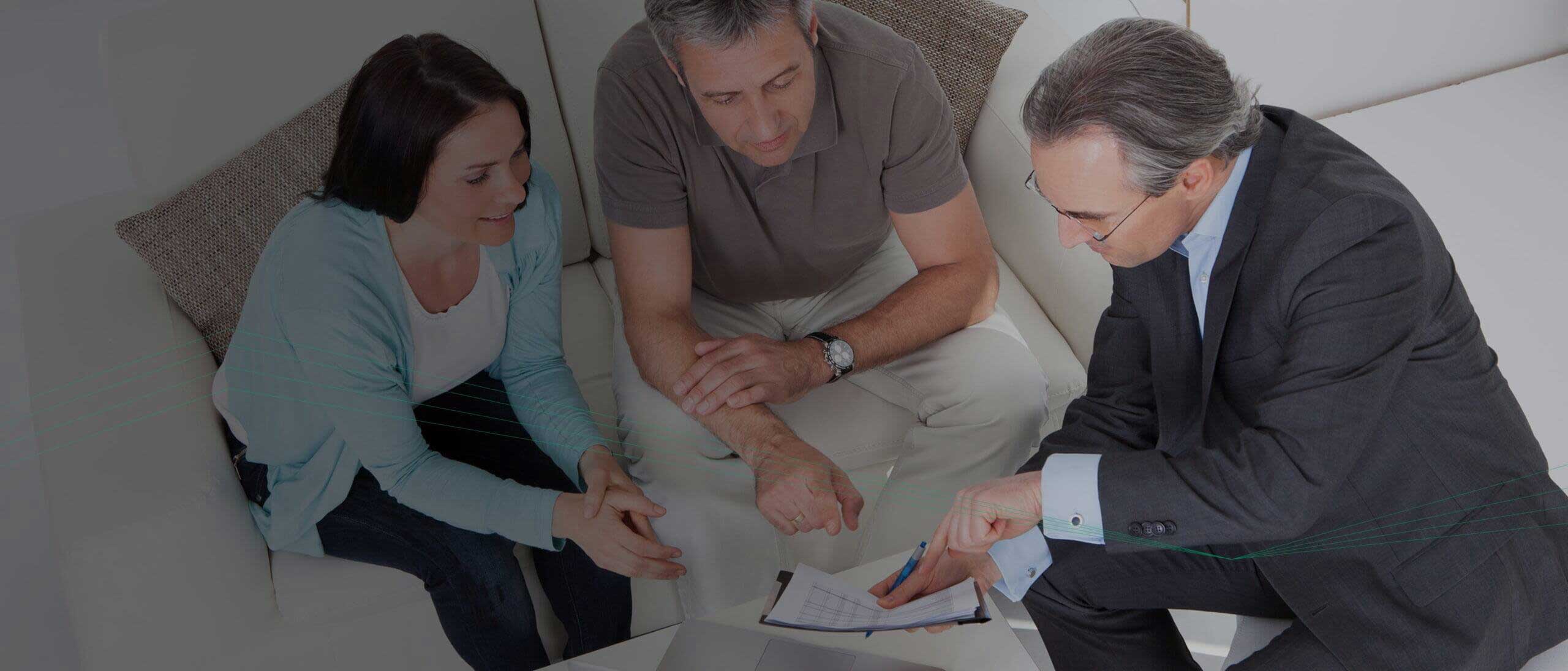 A couple sits on a couch while a man in a suit points to a document on a clipboard, discussing its contents, possibly outlining the features of Managed Detection and Response.