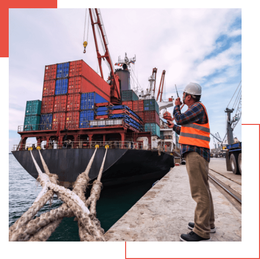  A worker in a reflective vest and hard hat stands on a dock beside a large cargo ship loaded with colored shipping containers, using a walkie-talkie to coordinate with the Managed Detection and Response team.