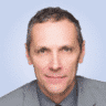  A man in a suit and tie, embodying the precision of a top SOC analyst, poses confidently against a light grey background.