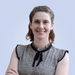  Woman with brown hair and a patterned blouse smiles at the camera, standing against a plain light blue background, embodying a sense of simplicity akin to streamlined MDR solutions.