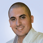  A person with a shaved head, wearing a light-colored collared shirt, smiles confidently at the camera against a light blue background, evoking the professionalism and trust often associated with top-tier MSSP services.