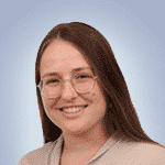  A person with long brown hair and glasses, perhaps a SecOps professional, smiles while wearing a beige top in front of a light blue background.