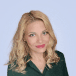  A person with long blonde hair, wearing a dark green top, is smiling slightly like they're sharing a secret about the latest MxDR advancements against a light blue background.