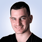  A person with short dark hair and a light skin tone smiles against a light blue background, embodying the calm confidence of someone who excels in the dynamic world of SecOps.