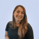  A person with long hair, smiling confidently in front of a plain light blue background, is wearing a dark shirt that hints at their expertise in SecOps.
