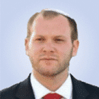  A man in a suit and red tie, wearing a kippah, stands against a plain background, embodying the professionalism and dedication of a SecOps expert.