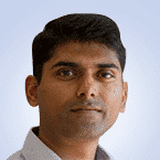  A man with short dark hair, wearing a light-colored collared shirt, looks directly at the camera against a light blue background, capturing the essence of confidence akin to an MSSP expert.
