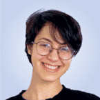  A person with short black hair and glasses smiles confidently at the camera against a light blue background, embodying the professionalism often seen in SecOps environments.