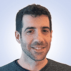  A person with short dark hair and a beard is slightly smiling against a light blue background, evoking the calm efficiency of an MxDR professional. They are wearing a dark gray sweater.