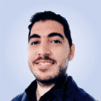  Smiling man with short dark hair and a beard, wearing a dark shirt against a light blue background, exudes confidence typical in the world of SecOps.