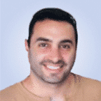  A person smiling, wearing a brown shirt, stands confidently against a light blue background, embodying the approachable expertise of an MSSP professional.