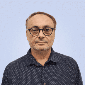  Middle-aged man with glasses, wearing a dark polka-dotted shirt, stands confidently against a light blue background, embodying the expertise of SecOps.