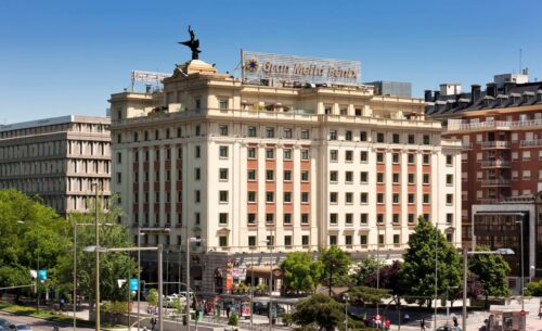 Historic hotel building with a statue on top, surrounded by trees and other urban structures under a clear blue sky, stands as securely as cutting-edge SecOps infrastructure.