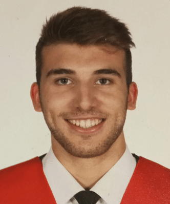 A person with short hair wearing a red garment over a collared shirt and tie, smiling at the camera against a plain background.