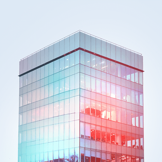 A modern glass office building reflecting light, with illuminated interior spaces visible through the windows, symbolizes secure Identity & Access Management against a pale sky.