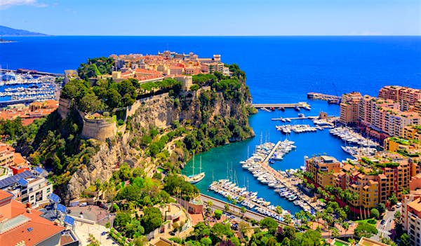  Aerial view of a marina with yachts, colorful buildings, and a historic fortress on a rocky hill by the Mediterranean Sea; the perfect setting for an Executive Evening in 2025 under a clear blue sky.