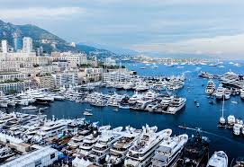  A harbor filled with numerous yachts and boats sets the scene for an exclusive Executive Evening, with city buildings and hills in the background under a partly cloudy 2025 sky.