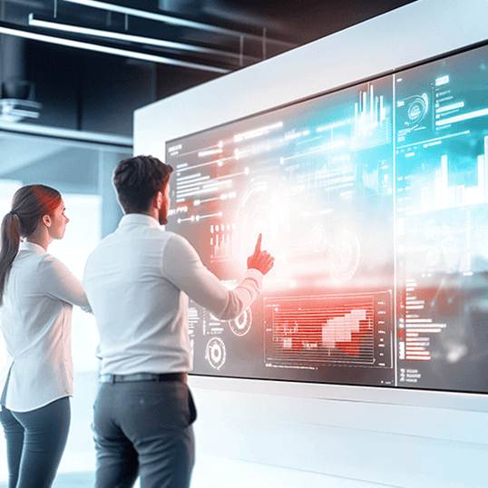  Two people interact with a large digital touchscreen displaying data visualizations, graphs, and charts—leveraging Agentic AI for deeper insights—in a modern office setting.