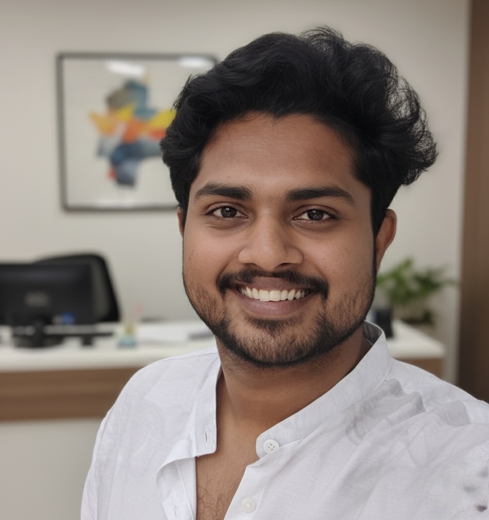  A man with dark hair and a beard wearing a white shirt smiles at the camera in an office setting.