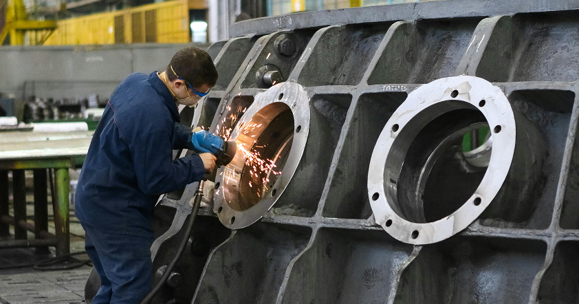 A worker wearing protective gear uses a power tool to grind the inside of a large metal industrial component, producing sparks—a key step in the manufacturing process.
