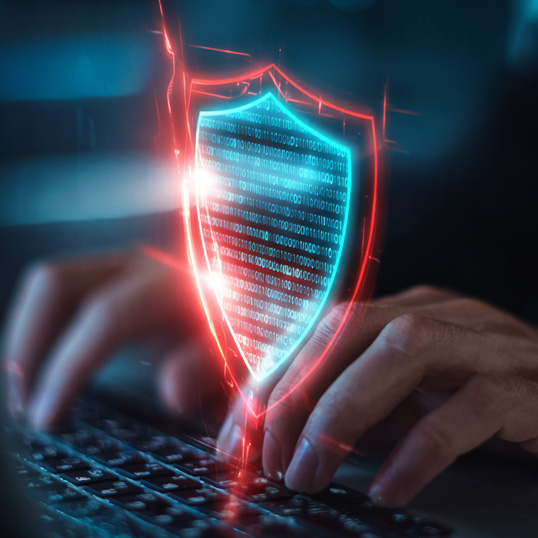  Hands typing on a keyboard with a digital shield displaying binary code, symbolizing cybersecurity, data protection, and highlighting the Security Skill Shortage in today's digital landscape.