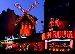 The Moulin Rouge cabaret in Paris is illuminated at night, featuring its iconic red windmill and bright neon signage—an unforgettable backdrop for an executive dinner.
