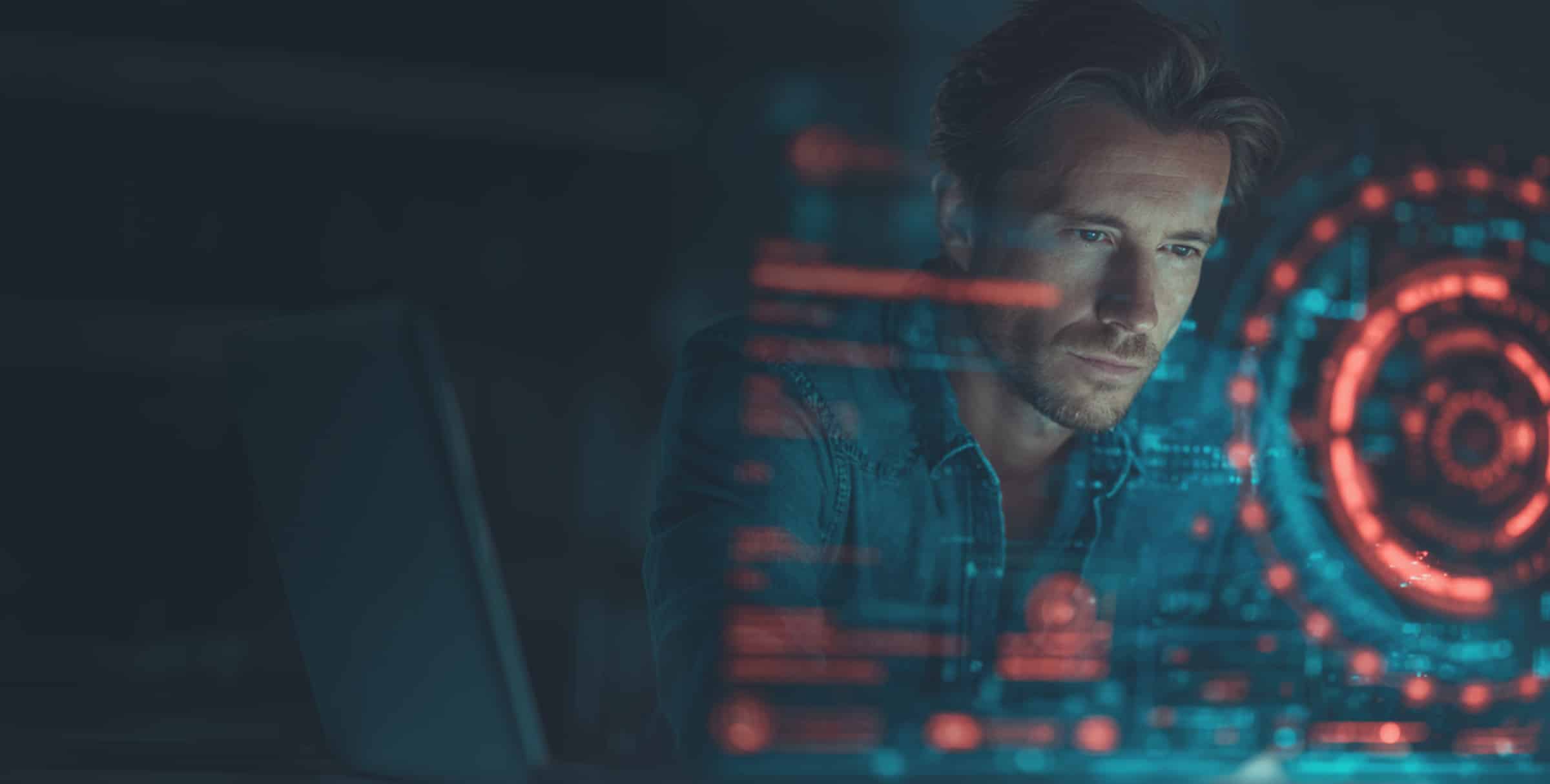 A man looks intently at a transparent digital interface displaying red and blue data graphics, with a laptop partially visible beside him.